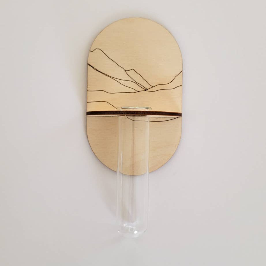 A wooden floral bouquet propagation wall holder mounted on a wall, with a glass tube attached.