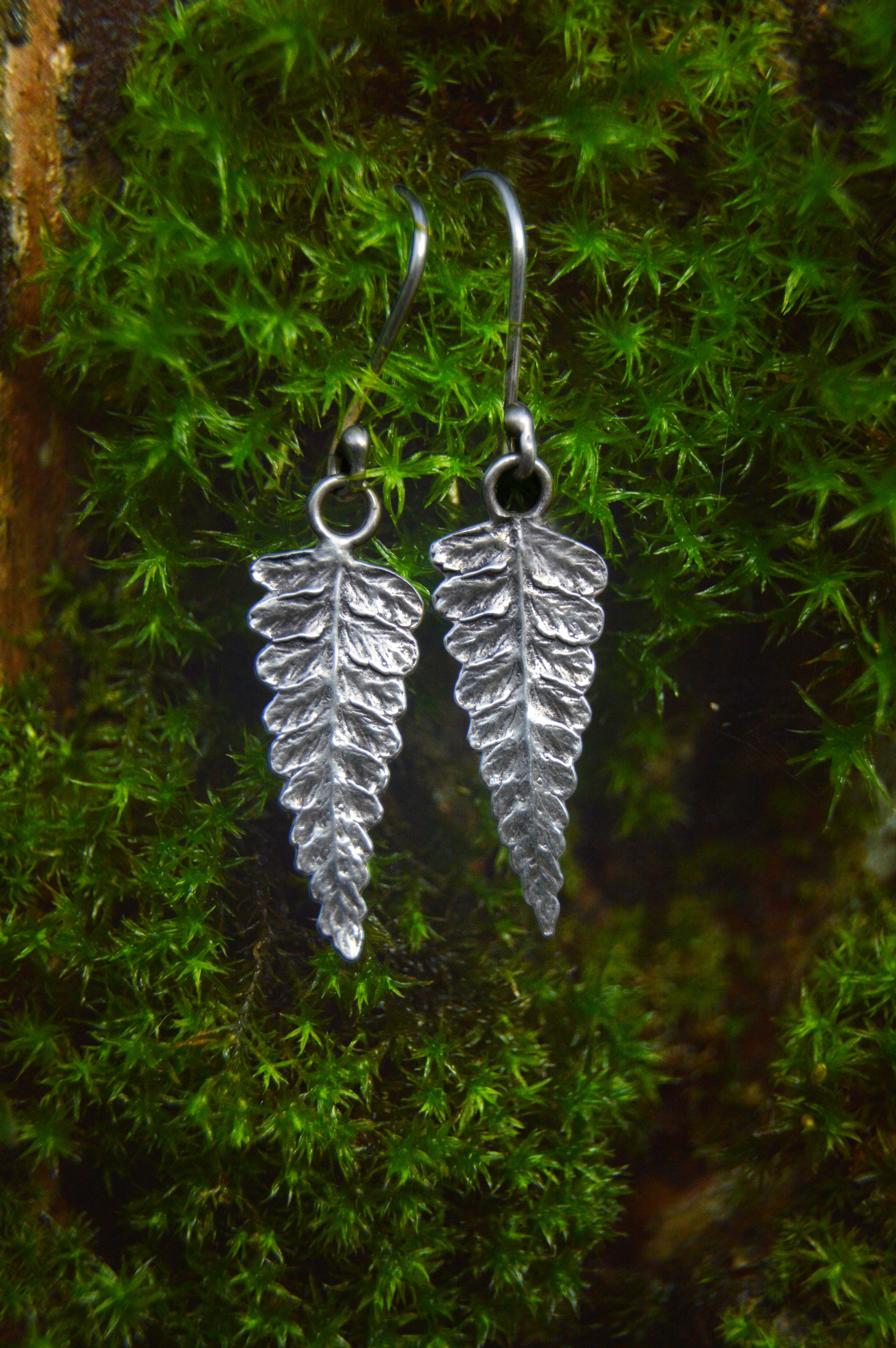 Silver leaf-shaped earrings on a green moss background