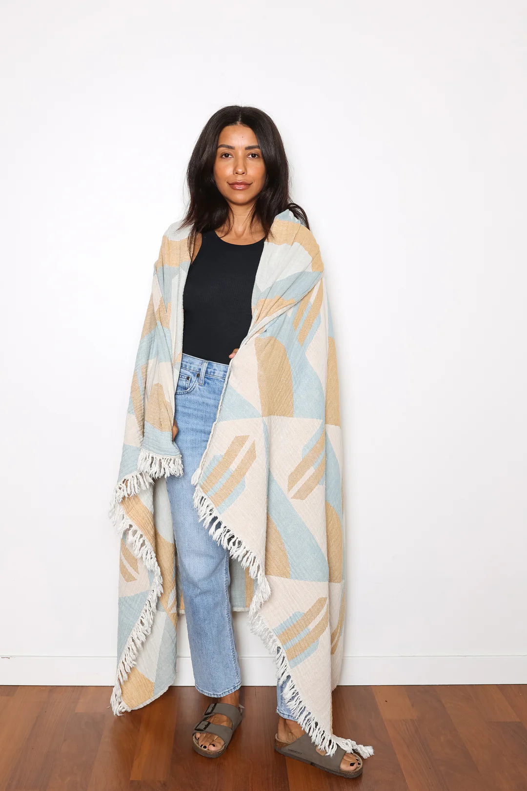 Woman wearing a patterned blanket draped over her shoulders against a white wall.