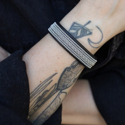 Close-up of a wrist wearing a silver bracelet with tattoos visible on the skin.